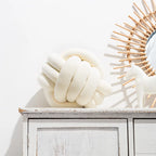 Coussin nœud en velours crème posé sur une commode blanche