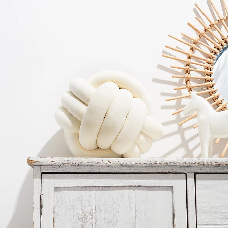 Coussin nœud en velours crème posé sur une commode blanche