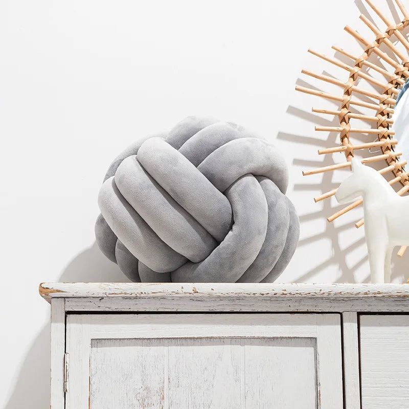 Coussin nœud en velours gris clair posé sur une commode blanche