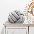 Coussin nœud en velours gris clair posé sur une commode blanche