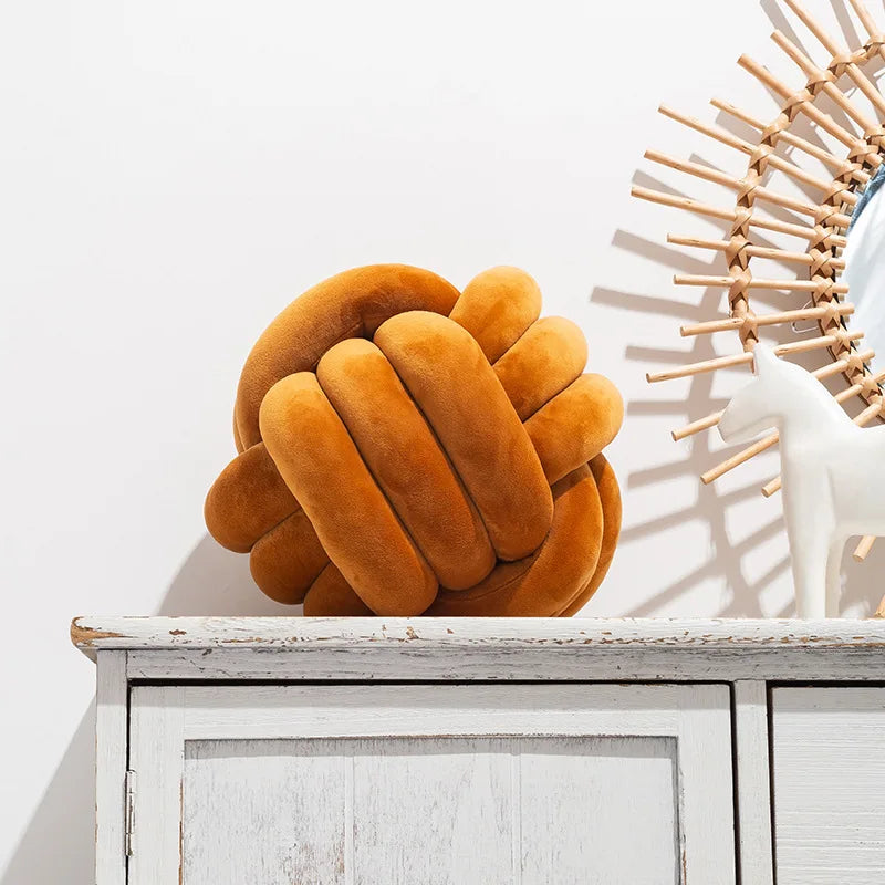 Coussin nœud en velours caramel posé sur une commode blanche