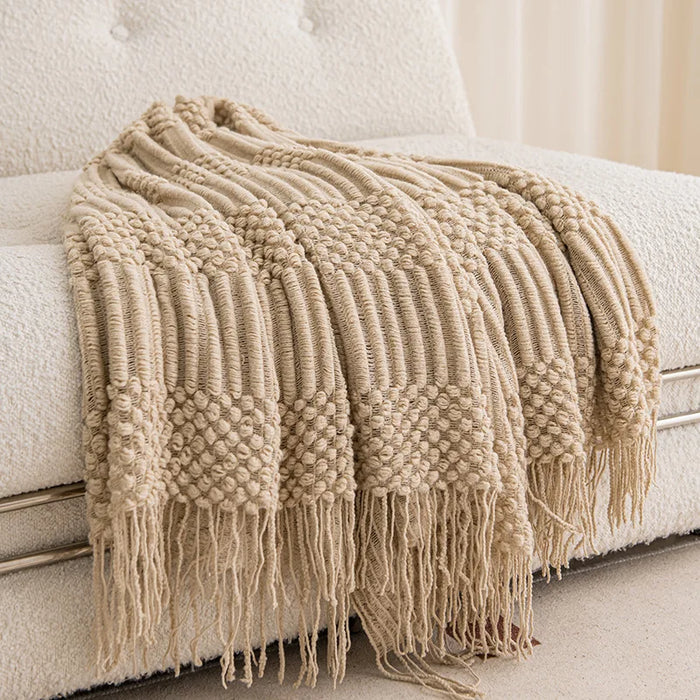 Plaid tricoté à franges beige sable drapé sur un canapé blanc