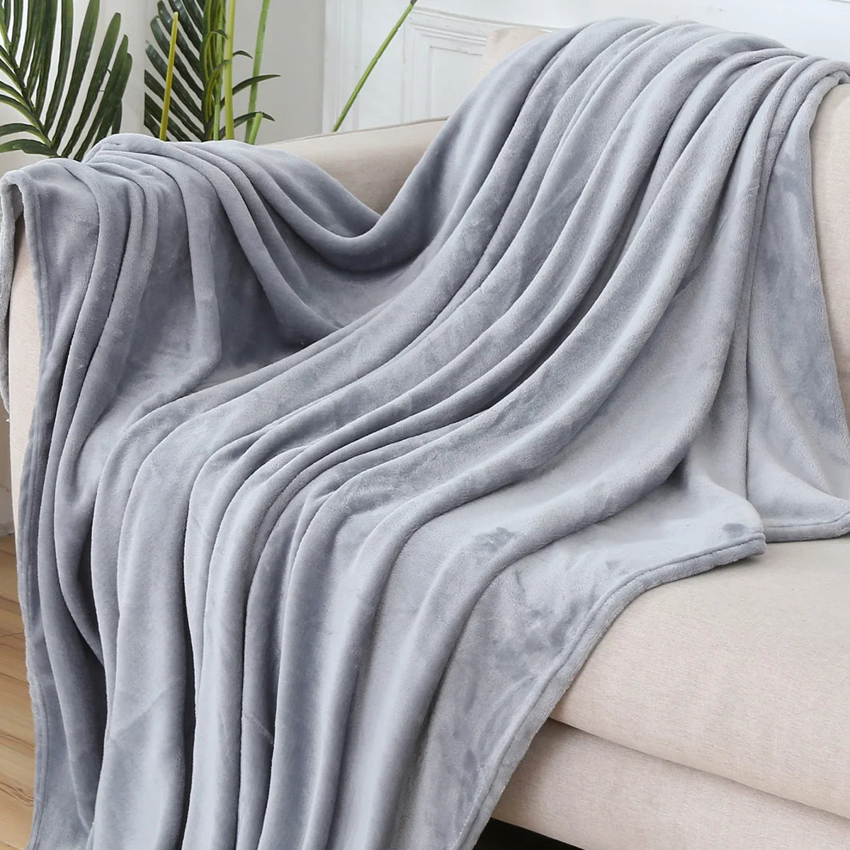 Plaid polaire uni gris clair drapé sur un canapé crème