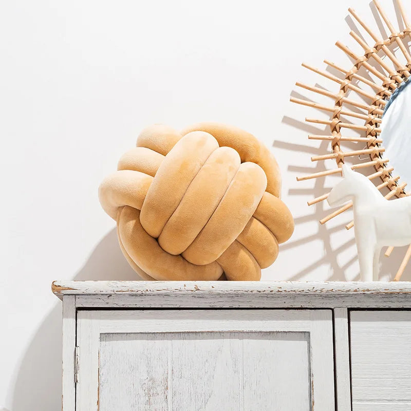 Coussin nœud en velours camel posé sur une commode blanche