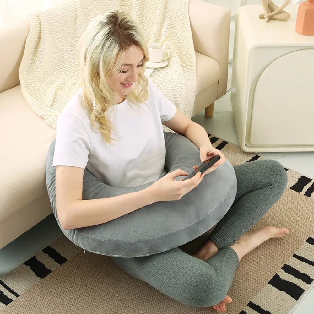 Coussin de lecture en C gris clair autour d’une femme assise par terre avec son téléphone