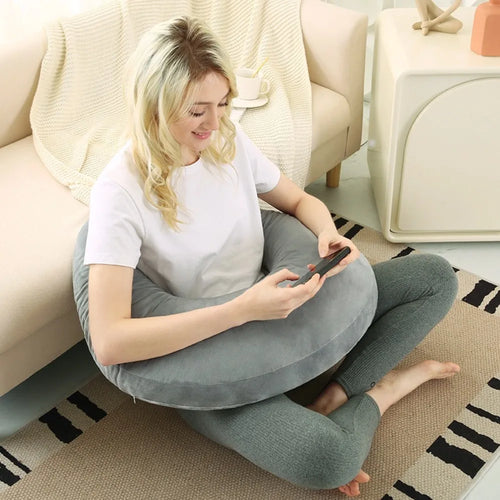 Coussin de lecture en C gris clair autour d’une femme assise par terre avec son téléphone