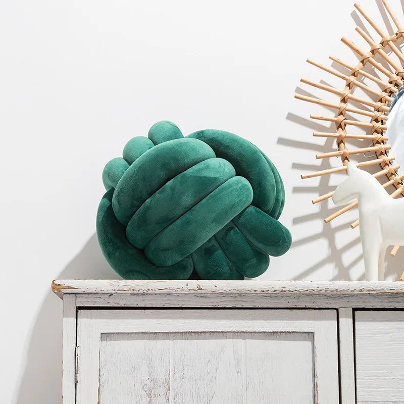 Coussin nœud en velours vert émeraude posé sur une commode blanche