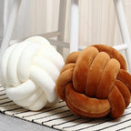 Coussins nœuds en velours crème et caramel posés sur un tapis rayé