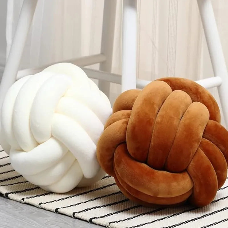 Coussins nœuds en velours crème et caramel posés sur un tapis rayé