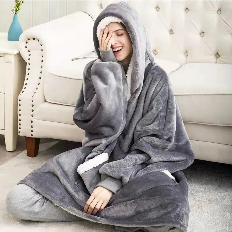 Femme assise au pied du canapé en sweat plaid extra long gris foncé, capuche sur la tête